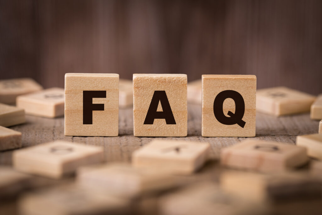 Three wooden blocks with the letters "F", "A", and "Q" arranged to spell "FAQ" are displayed on a wooden surface, with blurred letter blocks scattered in the background.