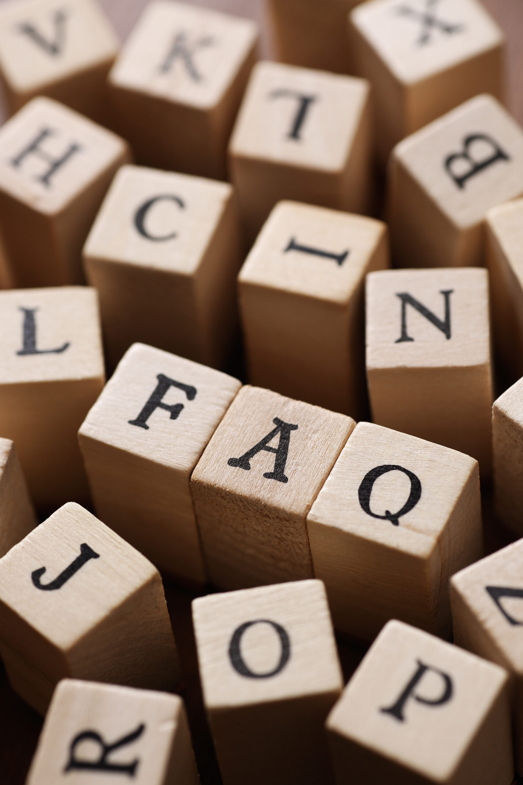 Close-up of wooden letter blocks with various letters visible. The central blocks clearly spell out "FAQ," standing out among the other scattered blocks.